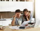 Unhappy American couple managing home accounts in kitchen, trying to save some money by cutting family expenses. Finances, bankruptcy, taxes, money, accounting and financial problems concept